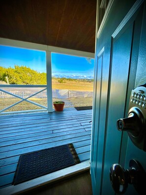 Una terraza de madera con vistas a un campo cercado y colinas al lejano.