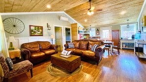 A spacious living room with leather sofas, a wooden ceiling, and a dining area with a kitchen in the background. - Prime Location in Dripping Springs! Gorgeous Country Cottage for 10 by Camp Lucy (Dripping Springs)