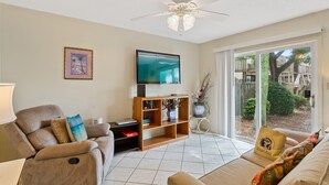 Un salon comprenant un canapé, un téléviseur, un ventilateur de plafond et une porte-fenêtre coulissante donnant sur un jardin.