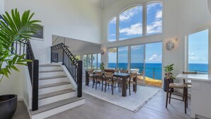 A spacious interior with a staircase leading to a balcony overlooking the ocean. - Honu Awa: Upscale Oceanfront Home w/ Pool, AC & Cliffside Views (Princeville)
