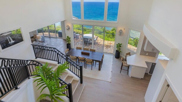 A spacious interior with a dining area, kitchen, and a large window overlooking the ocean. - Honu Awa: Upscale Oceanfront Home w/ Pool, AC & Cliffside Views (Princeville)