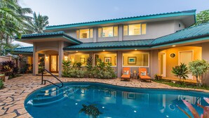 A two-story building with a swimming pool, outdoor seating, and tropical plants. - Honu Awa: Upscale Oceanfront Home w/ Pool, AC & Cliffside Views (Princeville)