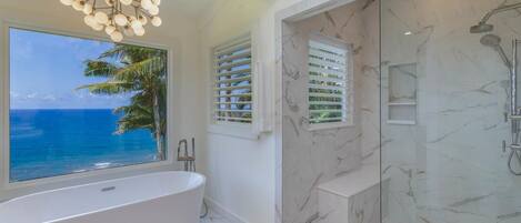 A modern bathroom with a freestanding bathtub, a glass-enclosed shower, and a view of the ocean through a large window.