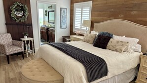 A bedroom with a large bed, a round ottoman, a dresser, a chair, and a mirror. - Amazing large Pool & Beautiful Desert Oasis in the Palm Desert area. (Palm Desert)