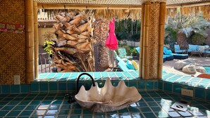 A bathroom with a sink, tiled floor, and a view of outdoor seating and palm trees. - Amazing large Pool & Beautiful Desert Oasis in the Palm Desert area. (Palm Desert)