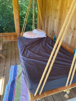 A wooden swing bed with ropes, a cushion, and a striped towel on a wooden deck.