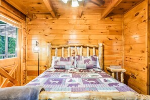 A wooden cabin room with a bed, a nightstand, and a window.
