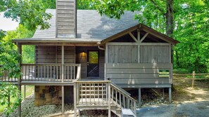 A rustic cabin with a porch, a chimney, and a small wooden structure attached to the main building.