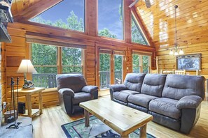 Ein gemütliches Blockhaus-Interieur mit Holzvertäfelung, einer Couch, einem Sessel, einem Tisch und einer Lampe.