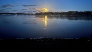 Een kalm meer in de schemering met een ondergaande zon die in het water weerspiegelt, omgeven door een bebost oever.