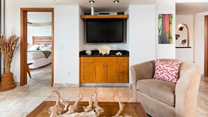 Un soggiorno moderno con una televisione a schermo piatto sopra un mobile in legno, un divano beige con un cuscino fantasia e un'originale scultura in legno sul pavimento.