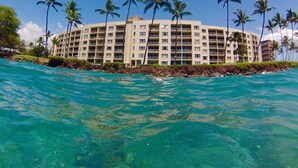 Un hotel sulla spiaggia con diversi piani, palme e acqua cristallina color turchese.