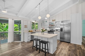 Una cocina moderna con una isla grande, electrodomésticos de acero inoxidable y vistas a vegetación exuberante.