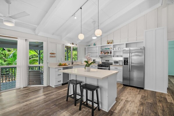 A modern kitchen with a large island, stainless steel appliances, and a view of lush greenery.
