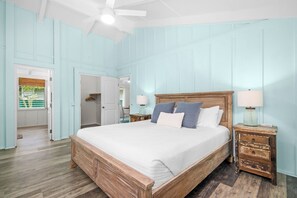 A bedroom with a large bed, wooden headboard, two bedside tables with lamps, and a ceiling fan.