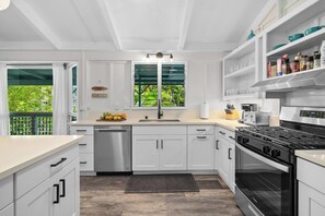 A modern kitchen with white cabinetry, a stainless steel dishwasher, a black stove, and a window with a view of greenery.