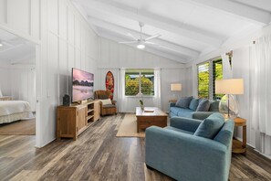 Amplia sala de estar con un sofá grande, una mesa de centro y un televisor. Se ve una ventana con cortinas y vistas al exterior con vegetación.