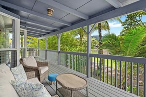 A covered outdoor area with wicker furniture and a view of lush greenery.