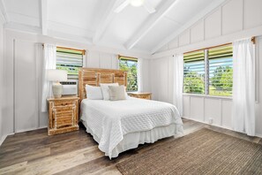 A bedroom with a wooden bed, white bedding, a bedside table with a lamp, and a view through the window.