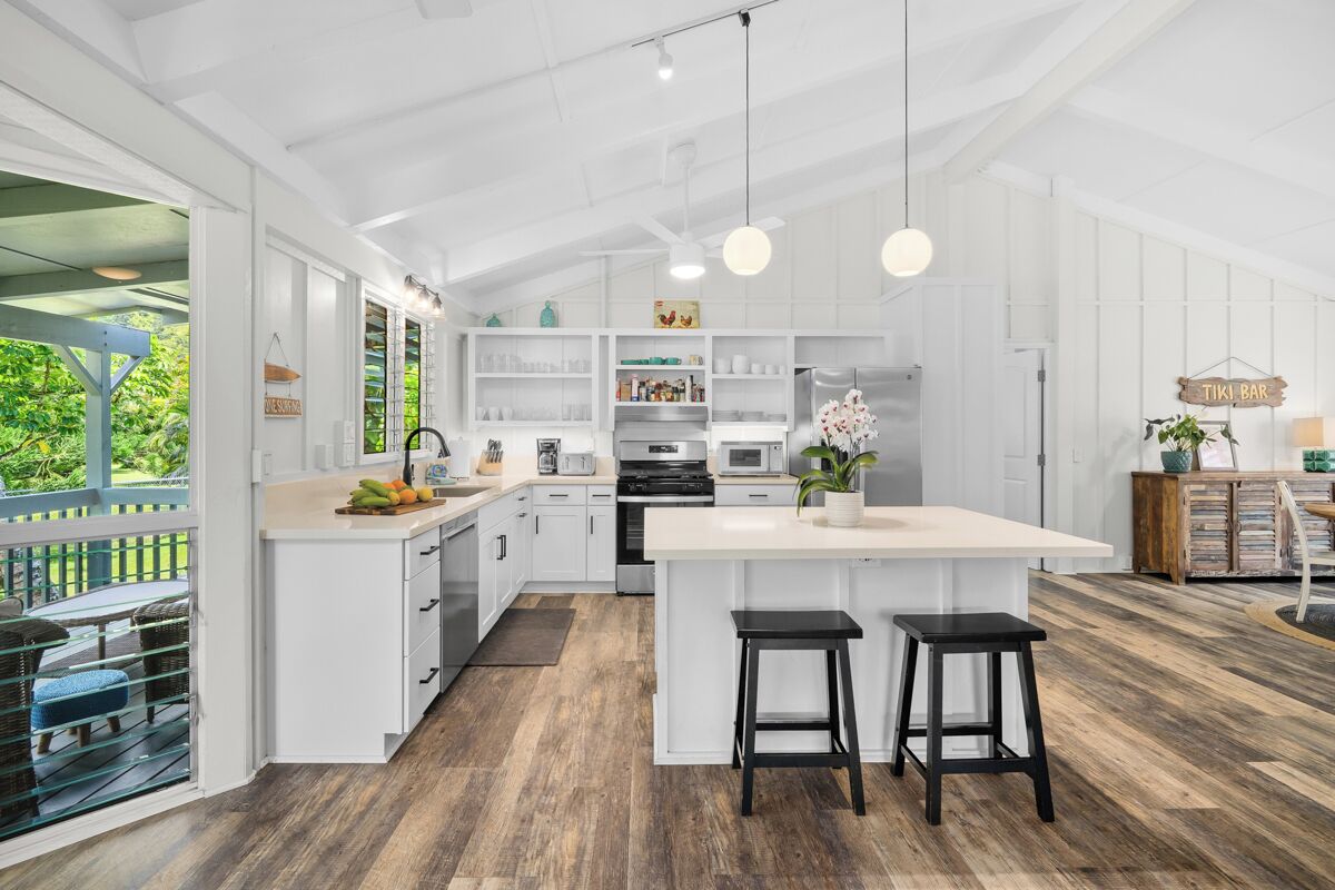 Cocina amplia con muebles blancos, una isla central con taburetes y vistas a zonas verdes.