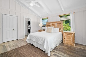 A bedroom with a large bed, a washing machine, a wooden headboard, and a window with curtains.