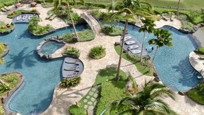 Ein Poolbereich eines Resorts mit verschiedenen Wasserelementen, darunter ein großer Pool, kleinere Whirlpools und eine Brücke, die die verschiedenen Bereiche miteinander verbindet.