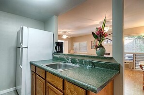 Compact kitchen area with refrigerator, sink, and countertop featuring a coffee maker and vase with flowers.