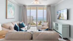 Ein Wohnzimmer mit großem Fenster, Deckenventilator, Sofa, Fernseher und Schrank.