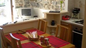 Un coin repas avec un mur en pierre, une table en bois agrémentée de sets de table rouges et un téléviseur posé sur un meuble.