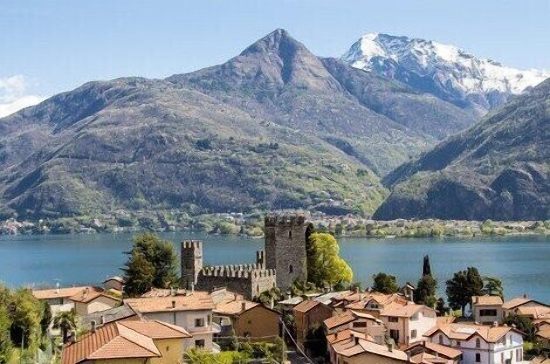 A town with traditional architecture, a castle, and mountains in the background.