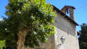 Un bâtiment rustique en pierre, doté d’un clocher, d’une porte en bois et d’un grand arbre devant.