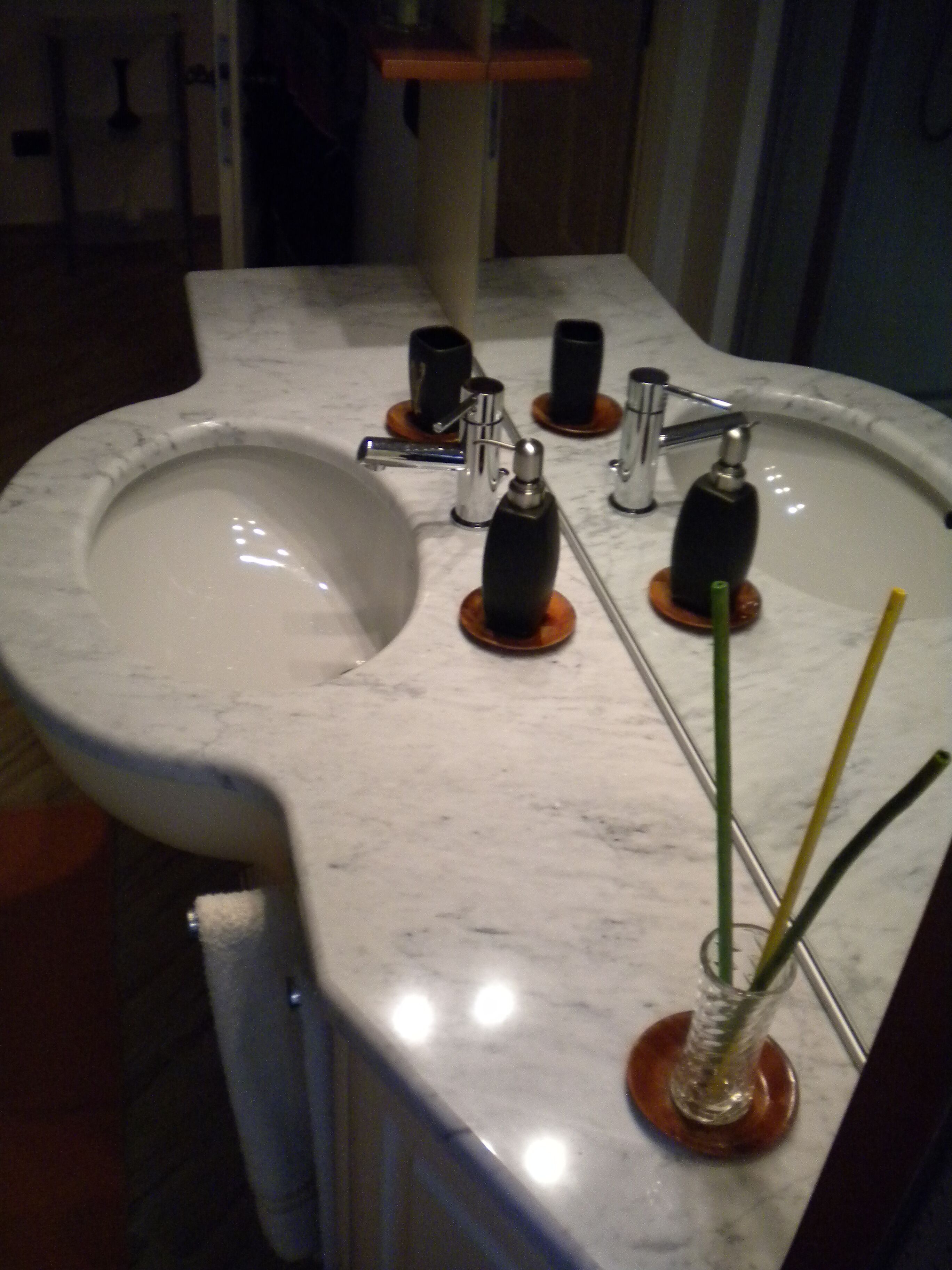 A bathroom sink with a marble countertop, a mirror, and a glass vase with a green reed.