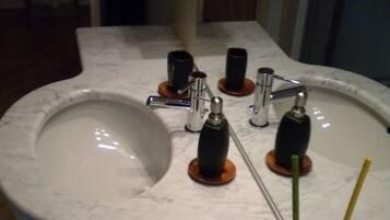 A bathroom sink with a marble countertop, a mirror, and a glass vase with a green reed.