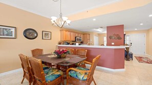 A dining area with wicker chairs and a glass-top table, a kitchen with wooden cabinets, and a living area with a red accent wall.