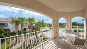 A balcony with a table and chairs, overlooking a residential area with palm trees and a house with a tiled roof. - Villas of Ocean Gate #208 Ocean side 2 bedroom, pool view, pet friendly (St Augustine)
