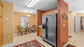 A kitchen with a stainless steel refrigerator, wooden cabinets, a dining table with chairs, and a window with blinds.