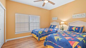 A bedroom with two beds, a ceiling fan, a window with blinds, and a wall sign.