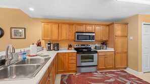 A compact kitchen with wooden cabinets, stainless steel appliances, and a red patterned rug.