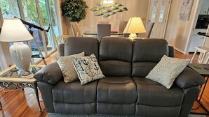 A dark leather sofa with patterned cushions, a glass coffee table, and a decorative plant. - Enjoy our new 16x25 screened in porch on Ocean Point Golf course (Fripp Island)