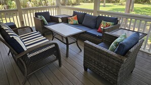 A covered outdoor seating area with wicker furniture and cushions, overlooking a lush garden. - Enjoy our new 16x25 screened in porch on Ocean Point Golf course (Fripp Island)