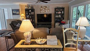 A living room with a sofa, a coffee table, a TV, and a bookshelf. - Enjoy our new 16x25 screened in porch on Ocean Point Golf course (Fripp Island)