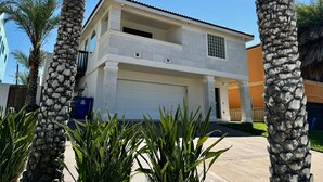 Een tweelaags huis met garage, omgeven door palmbomen en een helderblauwe lucht.