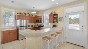 A modern kitchen with wooden cabinets, stainless steel appliances, a large island with bar stools, and a white door. - Walk to a public beach! Walk to restaurants! True Owner Operator. (Santa Rosa Beach)