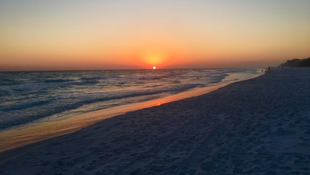 A beach with a sunset over the ocean, sandy shore, and a few people in the distance. - Walk to a public beach! Walk to restaurants! True Owner Operator. (Santa Rosa Beach)