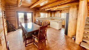 A spacious wooden cabin interior with a large dining table, chairs, a kitchen area, and a view through the open door. - Beautiful Lake-side 5 Bedroom Lodge (Altamont)