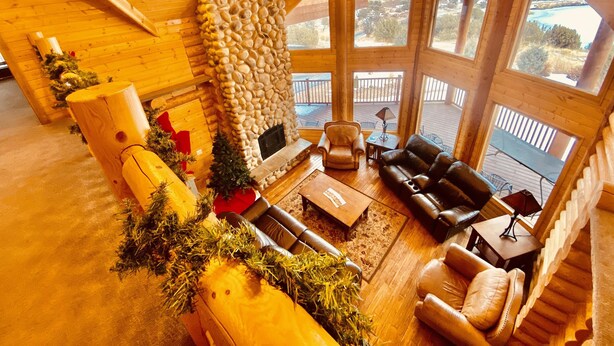 A cozy log cabin interior with a stone fireplace, leather sofas, and a balcony with a scenic view. - Beautiful Lake-side 5 Bedroom Lodge (Altamont)
