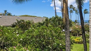 Un jardín tropical con palmeras, un edificio de techo inclinado y vista al océano.