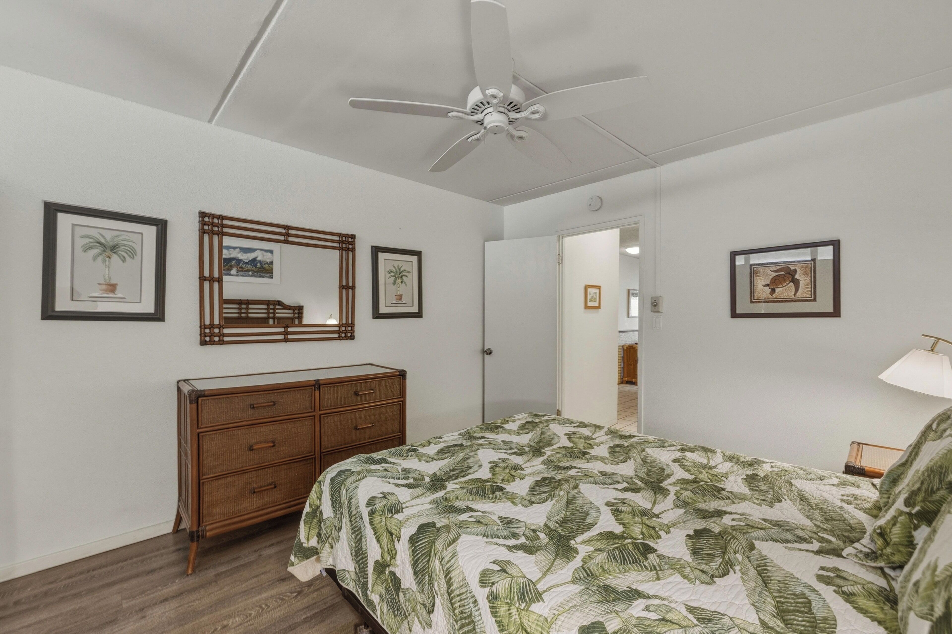 A bedroom with a bed, a dresser, a ceiling fan, and framed pictures on the walls.