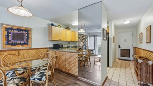 Una cocina con armarios de madera, un comedor con sillas de mimbre y piso de baldosas.