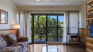 Habitación con ventilador de techo, sofá, televisor, balcón con sillas y vistas a zonas verdes.